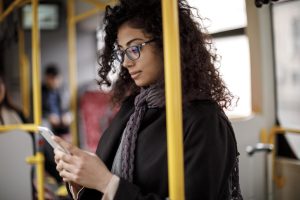 A woman is standing on a bus, using her mobile phone